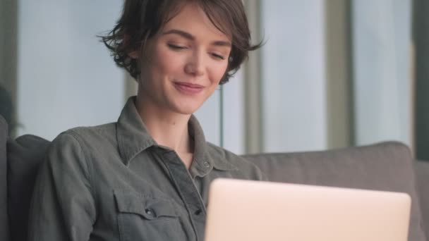 快乐的年轻漂亮的女人坐在沙发上 一边用笔记本电脑 一边环顾四周 — 图库视频影像