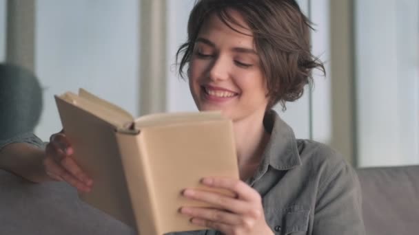 Ευτυχισμένη Νεαρή Όμορφη Γυναίκα Κοιτάζει Μακριά Στη Συνέχεια Διαβάζοντας Βιβλίο — Αρχείο Βίντεο