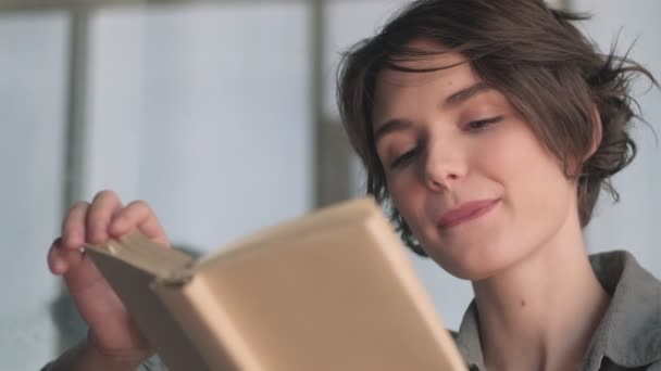 Sorrindo Jovem Bonita Mulher Lendo Livro Mordendo Lábios Enquanto Sentada — Vídeo de Stock