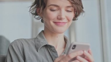 Evdeki kanepede otururken akıllı telefon kullanan tatmin olmuş genç bir kadın.