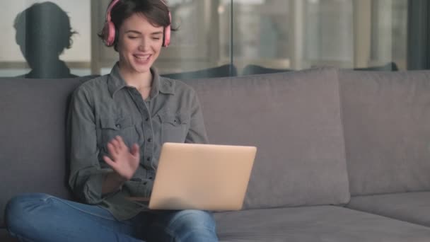Radosna Młoda Ładna Kobieta Słuchawkach Rozmawiająca Przez Video Laptopie Siedząc — Wideo stockowe