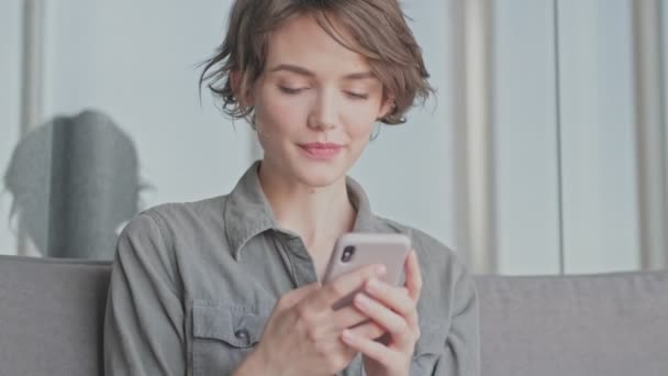 Sorrindo Jovem Bonita Mulher Usando Smartphone Mordendo Lábios Enquanto Sentada — Vídeo de Stock