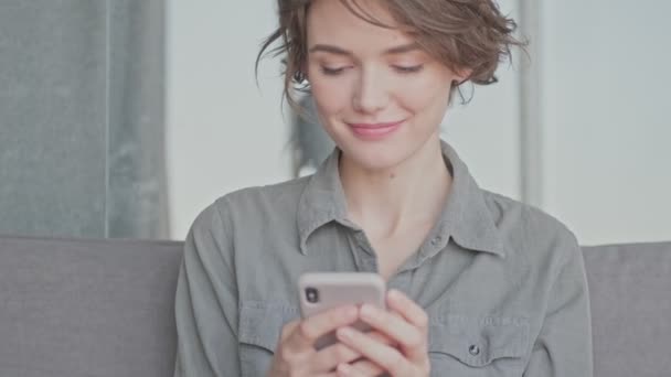 Agradável Jovem Bonita Mulher Usando Smartphone Enquanto Sentado Sofá Casa — Vídeo de Stock