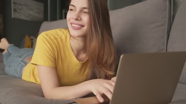 Zadowolona Młoda Kobieta Pisze Laptopie Leżąc Kanapie Domu — Wideo stockowe