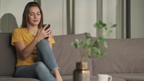 Fokusert Ung Kvinne Bruker Smarttelefonen Sin Mens Hun Sitter Sofaen – stockvideo