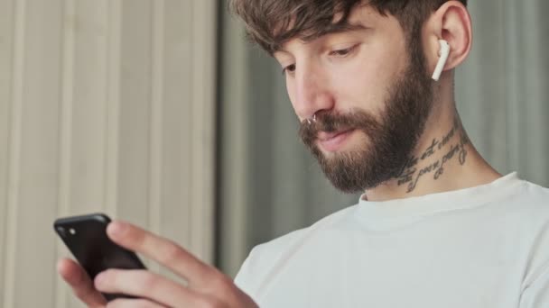 Stilig Ung Hipster Man Med Hörlurar Tittar Något Sin Smartphone — Stockvideo