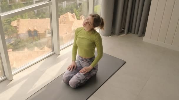 一位穿着运动服的年轻貌美的女士正在家里的一个健身垫上做伸展运动 — 图库视频影像