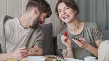 Gülümseyen, neşeli bir çift, erkek ve kadın evde birlikte kahvaltı ederken eğleniyor.
