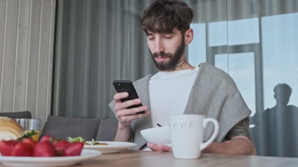 Sakin Genç Bir Hippi Kahvaltıda Akıllı Telefonunu Kullanıyor Evdeki Masada — Stok video