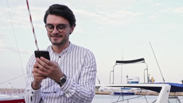 Ένας Όμορφος Νεαρός Που Φοράει Γυαλιά Χρησιμοποιεί Smartphone Του Ενώ — Αρχείο Βίντεο