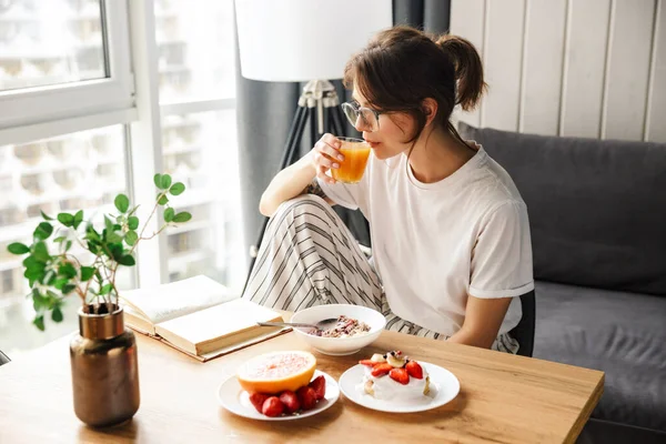 Photo Young Woman Reading Book Drinking Juice While Having Breakfast — Stock Photo, Image