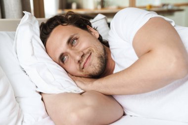 Yatakta yastığa uzanmış gülümseyen genç adam, dinleniyor.