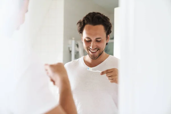バスルームミラーの前に立つ魅力的な幸せな若い男 歯をブラッシング — ストック写真