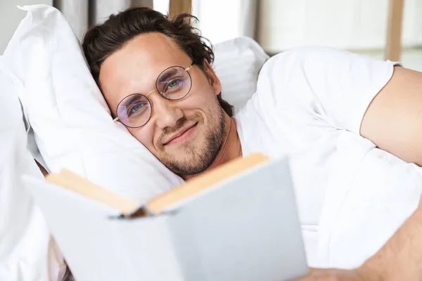 Jeune Homme Souriant Allongé Sur Oreiller Lit Lisant Livre — Photo