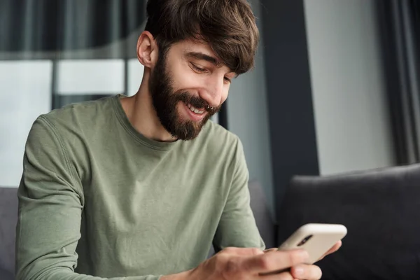 Image Handsome Joyful Man Smiling Using Mobile Phone While Sitting — Stock Photo, Image