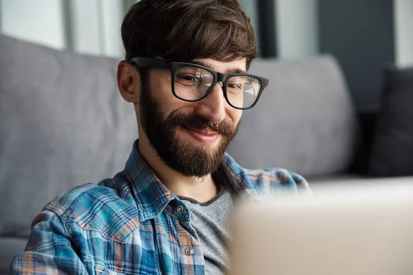 Imagem Homem Barbudo Feliz Óculos Sorrindo Usando Notebook Enquanto Sentado — Fotografia de Stock