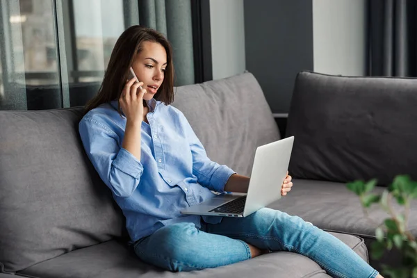 Bild Ung Fokuserad Kvinna Talar Mobiltelefon Och Använda Laptop Medan — Stockfoto