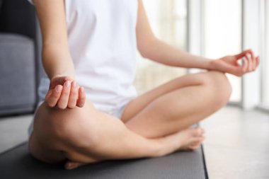 Kafkasyalı bir kadının, pencerenin yanındaki yoga minderinde otururken meditasyon yaptığı görüntüler.