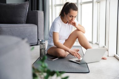 Kapalı bir pencerede mindere otururken not defteri ve cep telefonunda yazan esmer kadın resmi