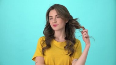 Sarı tişört giyen çekici genç bir kadın mavi arka planda tek başına duran bir şeyi düşünüyor ya da hayal ediyor.