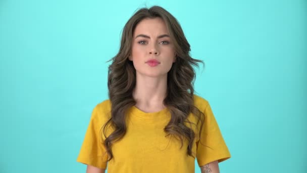 一位穿着黄色T恤衫的严肃的年轻女子正交叉着双手 摇着头 面对着被蓝色背景隔开的摄像机 — 图库视频影像