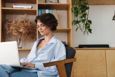Ofisteki sandalyede oturan ve dizüstü bilgisayarla çalışan kendine güvenen genç ve çekici bir girişimci.