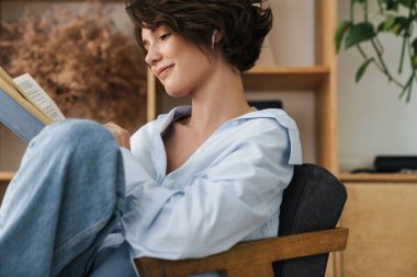 Ofiste otururken gülümseyen genç bir girişimci kadın kitap okuyor.