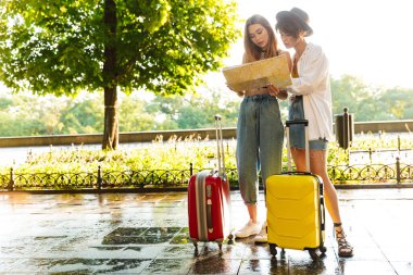 Green City Bulvarı 'nda elinde bavullarla durup haritaya bakan iki düşünceli genç kadının fotoğrafı.