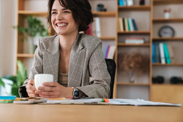 Bonita Sorridente Jovem Empresária Sentada Mesa Escritório Segurando Xícara Café — Fotografia de Stock