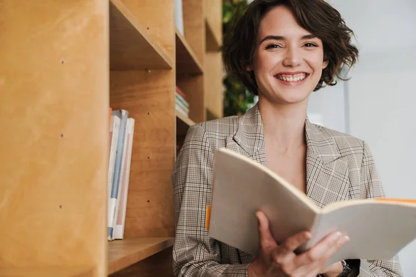 Lächelnde Junge Unternehmerin Liest Buch Während Sie Büro Bücherregal Steht — Stockfoto