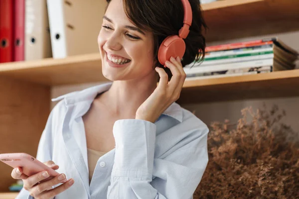 Leende Ung Kvinnlig Entreprenör Lyssnar Musik Med Hörlurar Och Mobiltelefon — Stockfoto