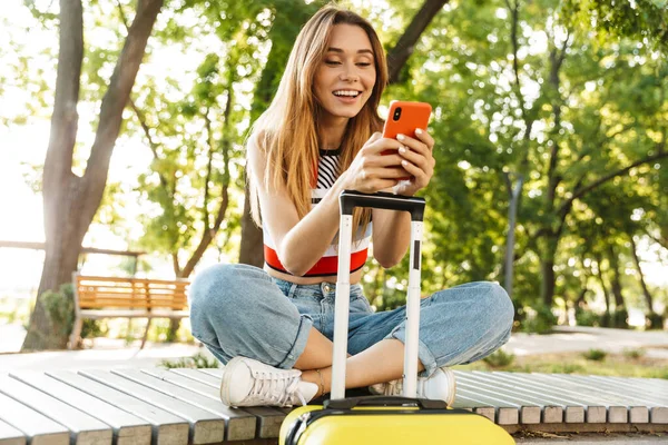 Foto Glad Turist Flicka Ler Och Håller Smartphone Medan Sitter — Stockfoto