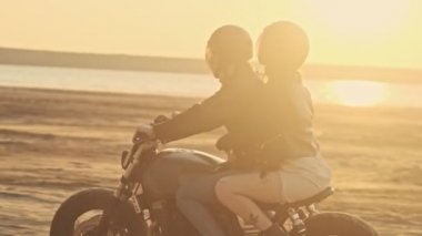 Çekici, mutlu bir çiftin yan görüntüsü. Erkek ve kadın gün batımında plajda motosiklet sürüyorlar.