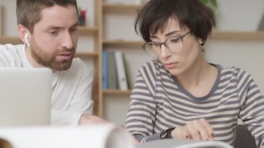 Odaklanmış meslektaşlar modern ofiste dizüstü bilgisayarlarla yürürken konuşuyorlar ve belgeler okuyorlar.