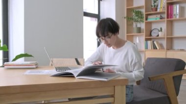 Genç ve güzel bir iş kadını modern ofiste kağıt belgeler ve dizüstü bilgisayar kullanarak çalışıyor.