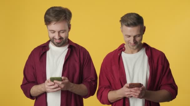 两个迷人的成年人用他们的智能手机站在黄色的背景下 — 图库视频影像