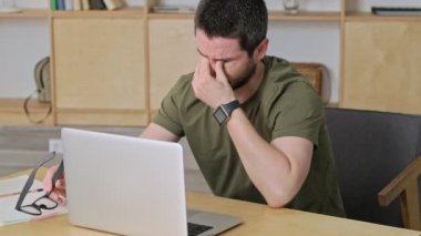 Yorgun bir genç adam iş sırasında laptopuyla gözlerini kapatıyor.