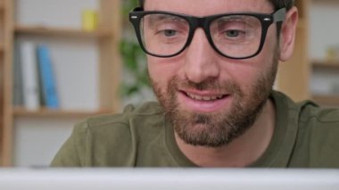 Gözlüklü yakışıklı bir iş adamının yakın plan görüntüsü ofiste dizüstü bilgisayarıyla oturuyor.