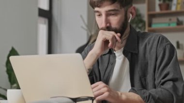 Ciddi bir genç dijital sanatçı ofiste dizüstü bilgisayarıyla çalışırken bir şeyler yazıyor.