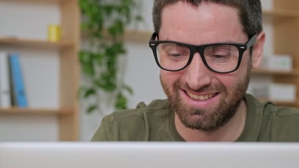一位成功的年轻商人戴着眼镜 与他的笔记本电脑坐在办公室的桌子旁 这是一张近照 — 图库视频影像