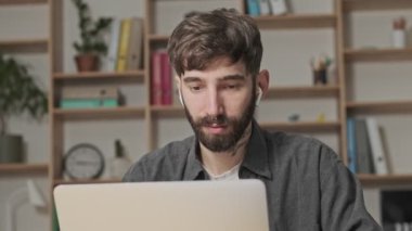 Kulaklık takan genç ve çekici bir dijital sanatçı ofiste oturmuş bilgisayarını içerken bilgisayarına bakıyor.