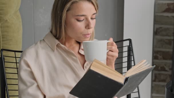 Calmo Mulher Loira Atraente Ler Livro Beber Chá Enquanto Sentado — Vídeo de Stock