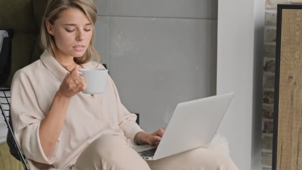 在家里坐在椅子上 用笔记本电脑喝茶 让迷人的金发女人冷静下来 — 图库视频影像