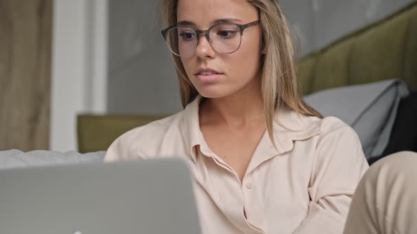 在家里坐在地板上的时候 用笔记本电脑对着眼镜的漂亮金发女人进行了聚焦 — 图库视频影像