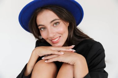 Güzel, iyimser, mutlu, mavi şapkalı bir kadının görüntüsü. Beyaz duvar arkasında izole bir şekilde poz veriyor..