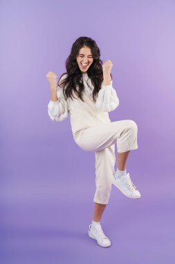 Mor duvar arkasında yalnız poz veren mutlu, iyimser, genç esmer kadın imajı kazanan hareketi yapar.