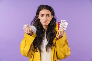 Mor duvar arkasına izole edilmiş hasta bir kadın resmi. Elinde peçete ve haplar var..