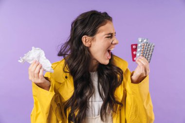 Mor duvar arkasına izole edilmiş, elinde peçete ve haplarla hasta ve stresli bir kadın resmi..