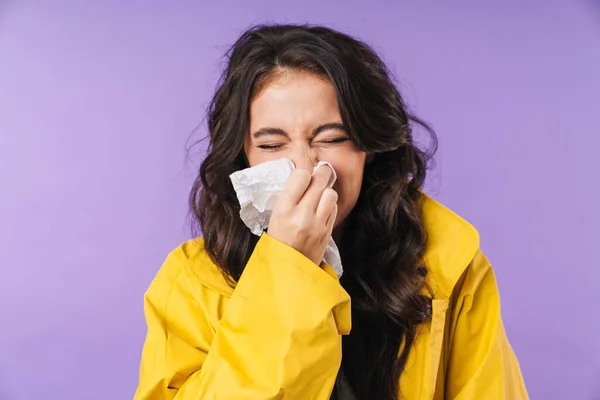 Image of ill sick woman sneeze isolated over purple wall background holding napkin.