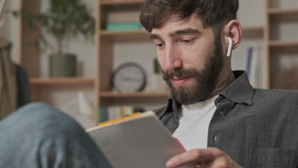 Närbild Glad Ung Hipsterman Med Hörlurar Läser Anteckningar Sin Copybook — Stockvideo